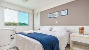 A modern bedroom with a large bed, a bedside table, a chair, and a window with a view of greenery. - Bz73 Geribá! Casa c/ piscina privativa 5 Suítes! (Búzios)