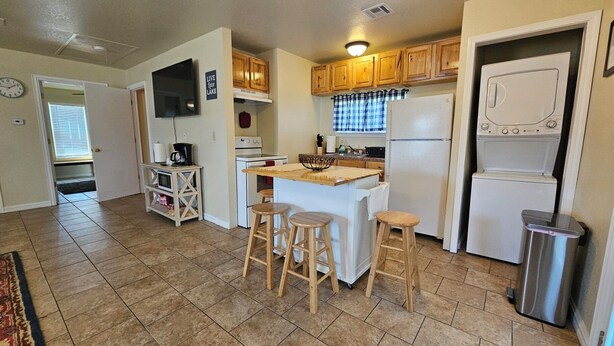 A compact kitchen with wooden cabinets, a microwave, a stove, and a refrigerator. There are three stools around the island. - Heart of Disney House - Easy Trail Access (Disney)