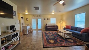 A cozy living room with a sofa, coffee table, and a rug. There is a kitchen area with stools and a coffee maker. - Heart of Disney House - Easy Trail Access (Disney)