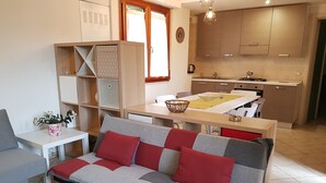 A modern living room with a sofa, a dining table, and a kitchen area.