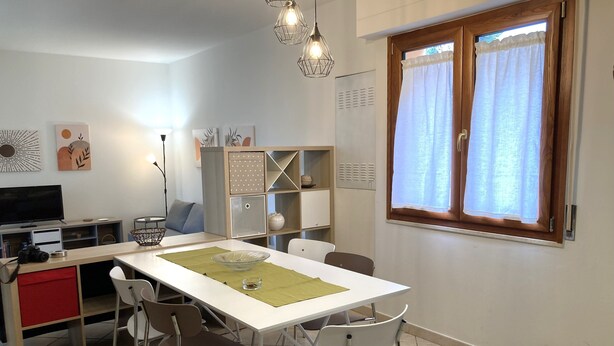 A modern kitchen with a dining table, chairs, a TV, and a bookshelf.
