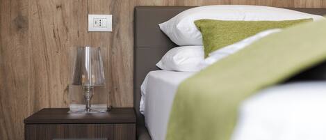 A neatly made bed with white and green bedding, a bedside lamp, and a wooden nightstand with a drawer.