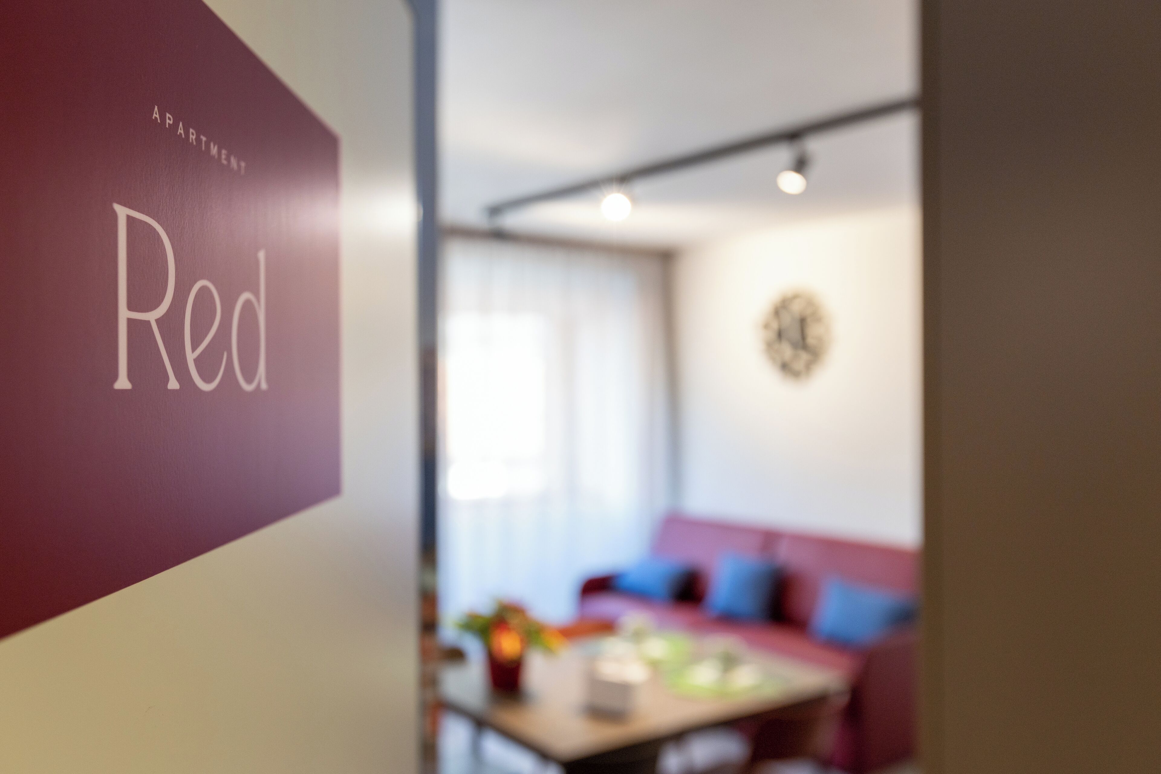 Ein verschwommener Innenraum einer Wohnung, auf einer Wand ist ein Schild mit der Aufschrift 'Apartment Red' zu sehen.