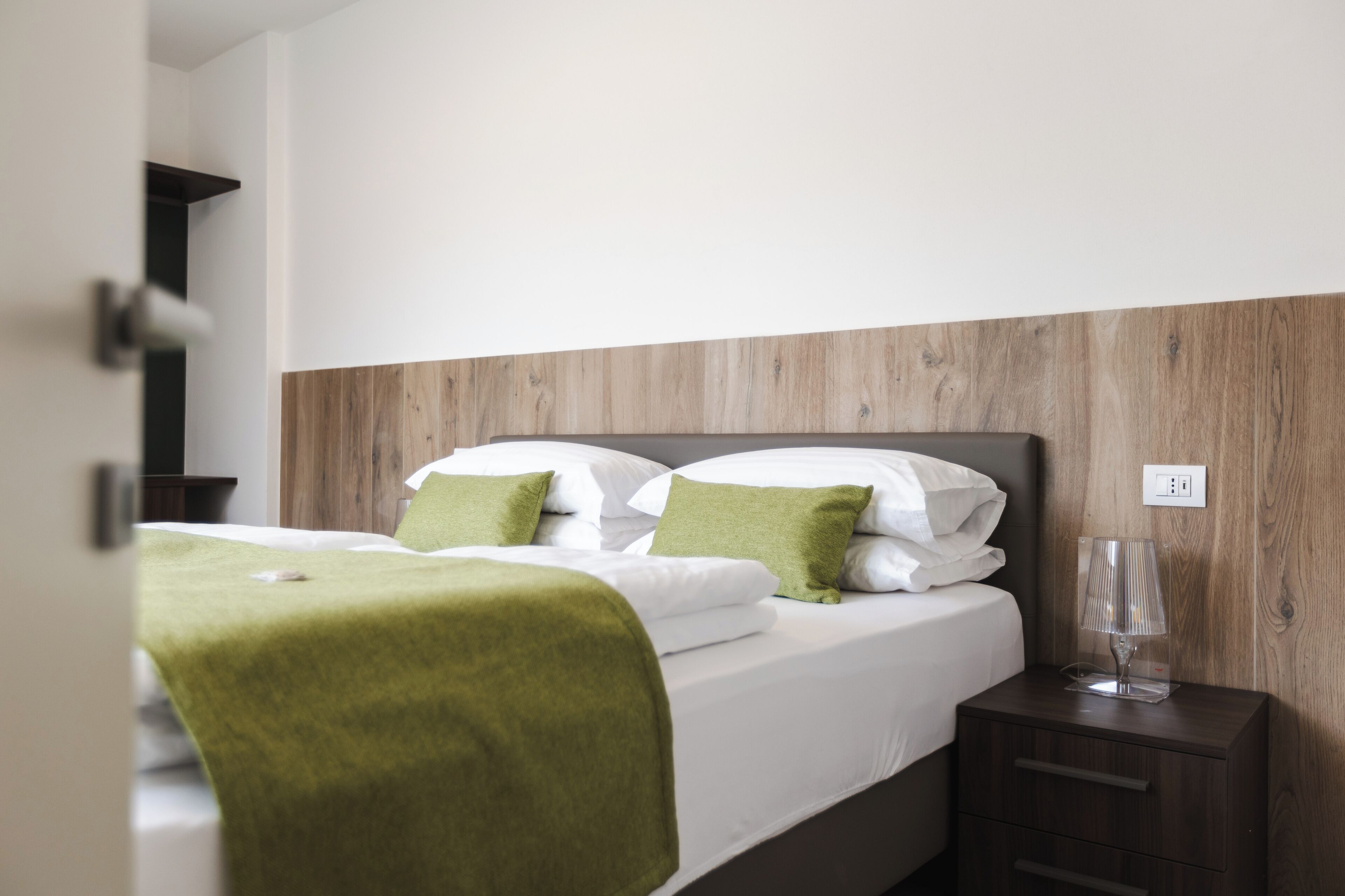 Una cama bien hecha con almohadas verdes, una lámpara de noche y un cabecero de madera.