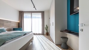 A modern hotel room with a large bed, a small seating area, a television, and a window with curtains. - Boutique Apartments By Annalisa (Nago-Torbole)