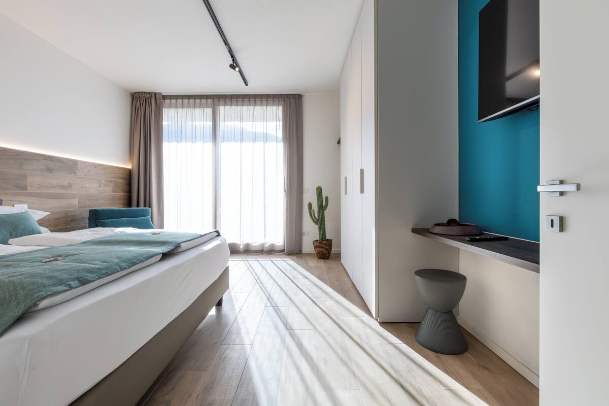Moderni hotellihuone, jossa on suuri sänky, pieni oleskelualue, televisio ja ikkuna, jossa on verhot.