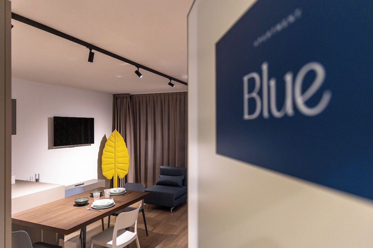 Una habitación de hotel moderna con zona de comedor, un gran ventanal y una cortina.