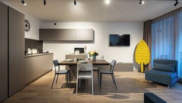 A modern kitchen with a dining area, a flat-screen TV, and a large decorative plant.