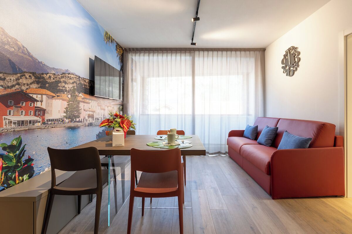 Una sala de estar moderna con comedor, un sofá rojo y vista a un cuerpo de agua a través de una ventana.