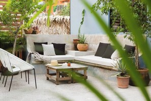 A cozy outdoor seating area with a white sofa, a wooden table, and various potted plants.