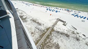 En strand med en lång brygga som sträcker sig ut i vattnet, ett sandigt strandområde med parasoller och en fri utsikt över havet.