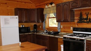 A cabin-style kitchen with wooden cabinets, a refrigerator, a microwave, a stove, and a sink. - Handicap Cabin with hot tub ~ NO PETS (Clarington)