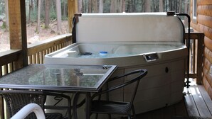 A hot tub with a control panel, a glass table, and two chairs on a wooden deck. - Handicap Cabin with hot tub ~ NO PETS (Clarington)