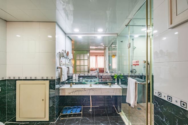 Un baño moderno con cabina de ducha de vidrio, tocador con lavabo de vidrio y suelo de mármol.