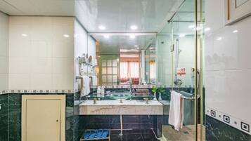 Un baño moderno con cabina de ducha de vidrio, tocador con lavabo de vidrio y suelo de mármol.