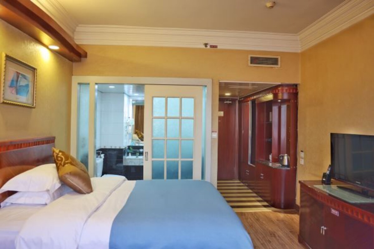 A hotel room with a bed, a television, a wardrobe, and a bathroom visible through an open door.