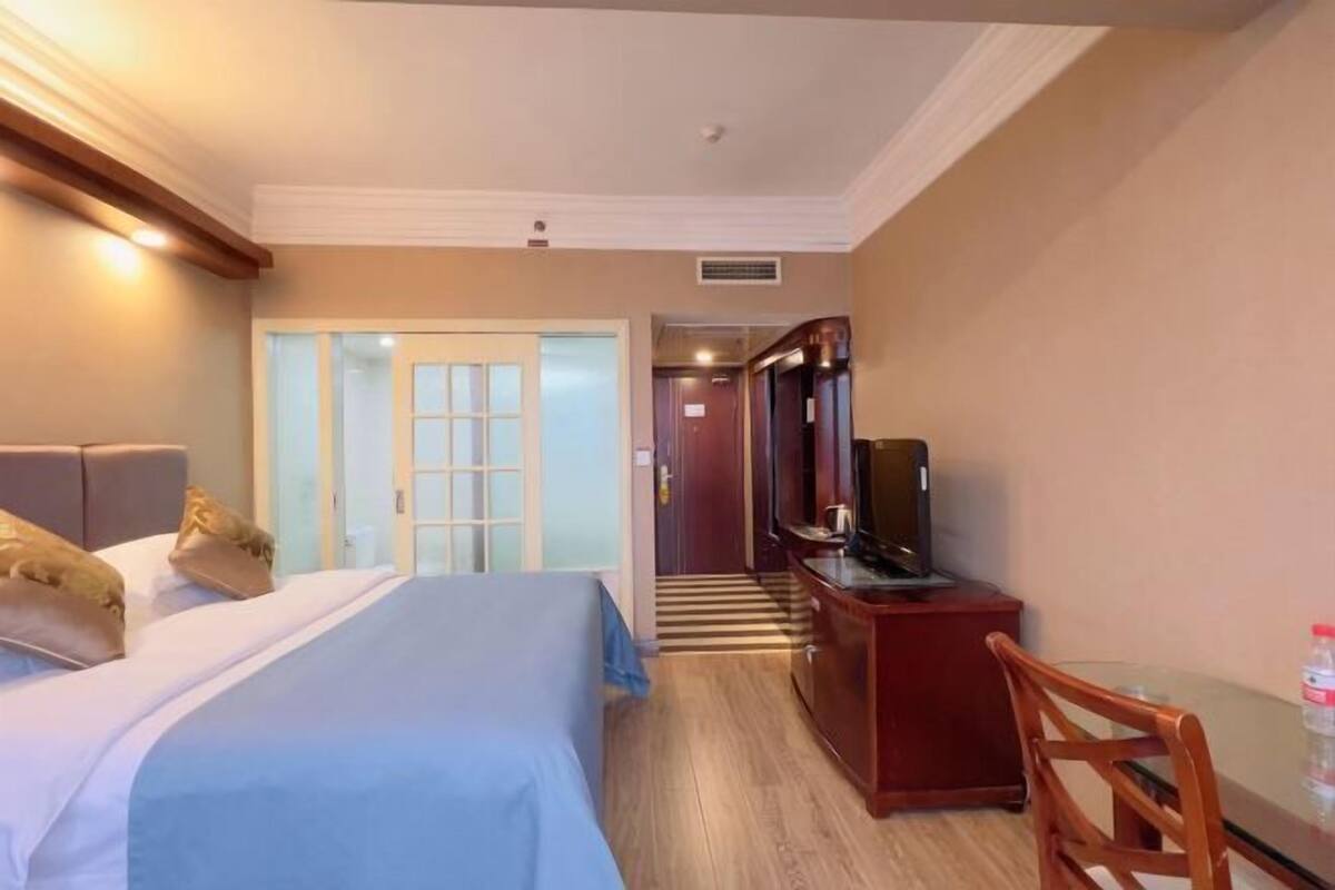 A hotel room with a bed, a desk with a television, a chair, and a door leading to another room.