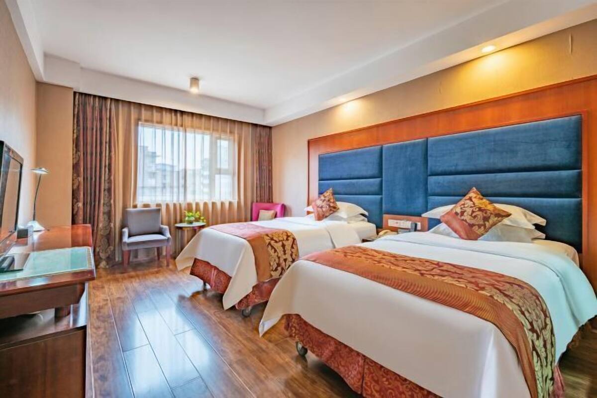 A hotel room with two beds, a desk, a chair, and a window with curtains.