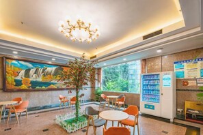 A hotel lobby with a mural, a vending machine, and seating arrangements. - Jinye Hotel (zhanggongqiao Food Street) (Leshan)