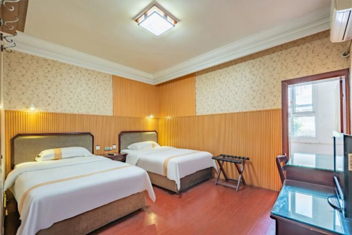 A hotel room with two beds, a small table, a chair, and a TV.