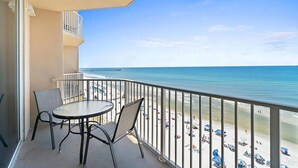 Ein Balkon mit Tisch und Stühlen mit Blick auf einen Strand mit Sonnenschirmen.