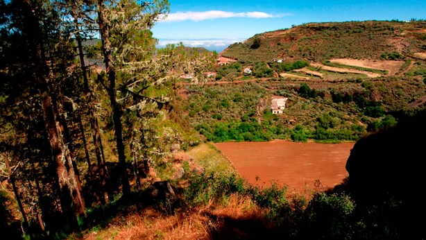 Paisagem rural com estrada de terra, árvores e algumas construções espalhadas.