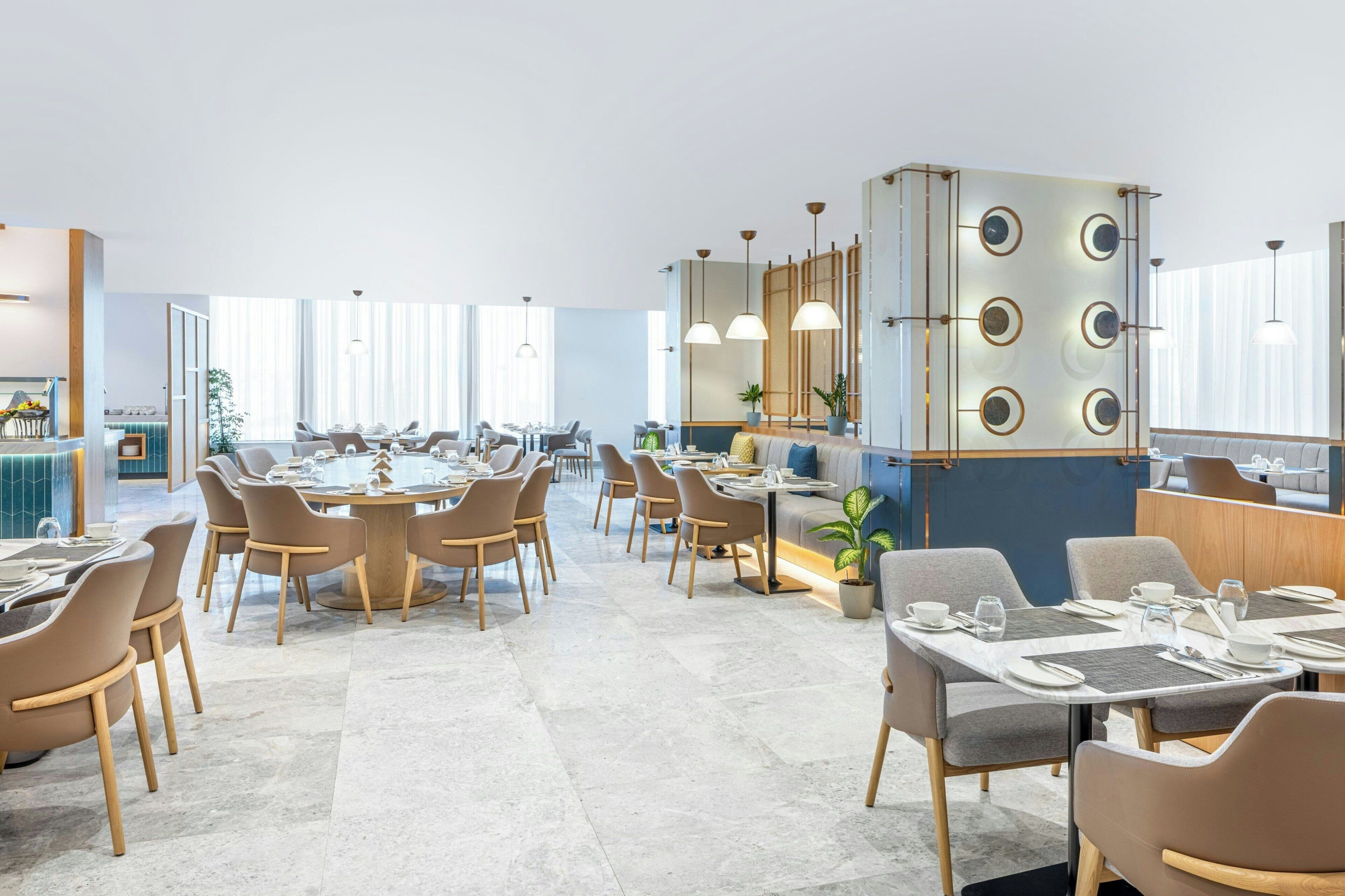 A modern dining area with round tables and chairs, a central decorative column, and pendant lighting.