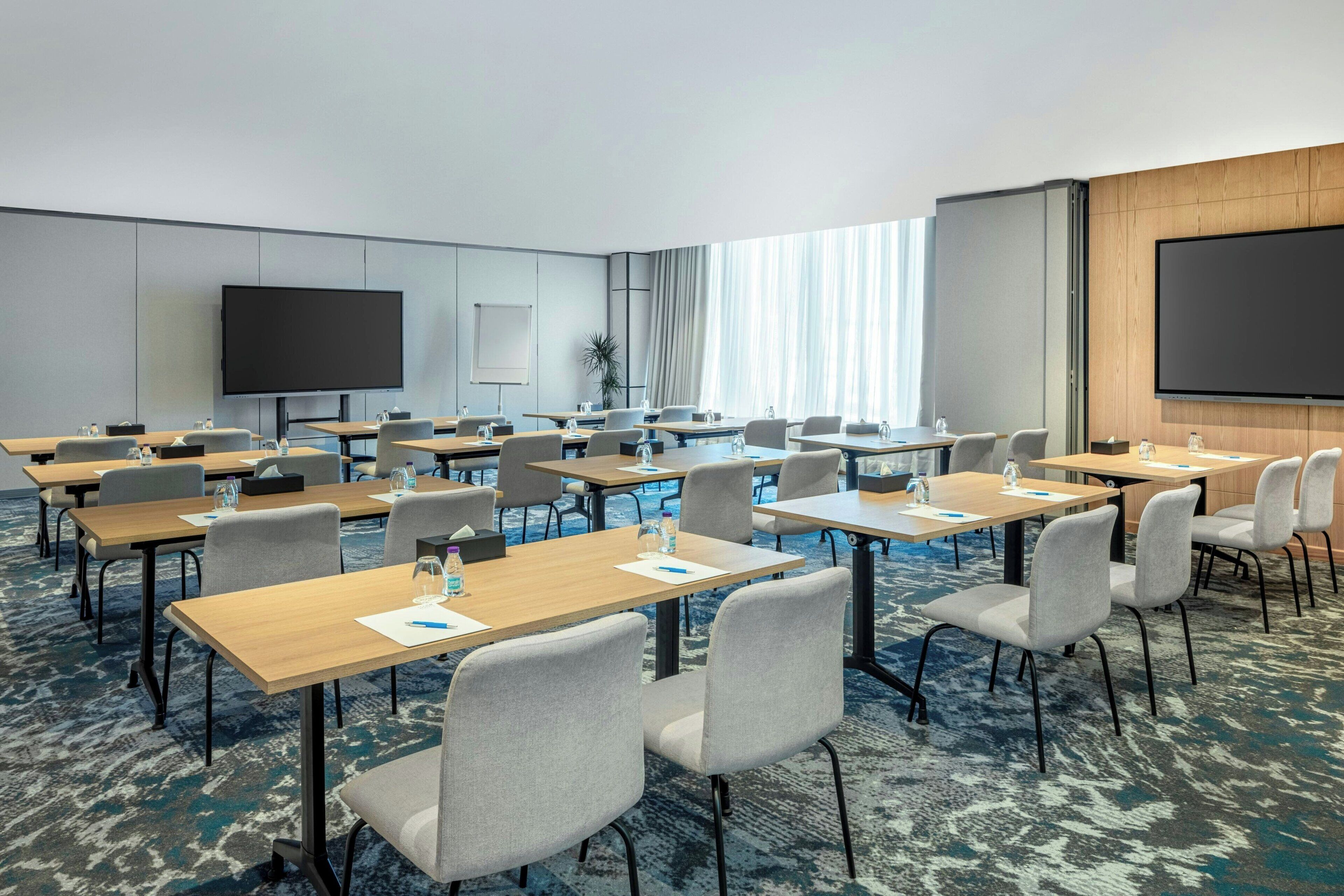 Un salón de conferencias con varias mesas y sillas, una pantalla grande y una pizarra.