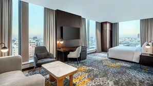 A hotel room with a large bed, a desk, a TV, and a view of the city. - Four Points By Sheraton Jeddah King Fahd Road (Jeddah)