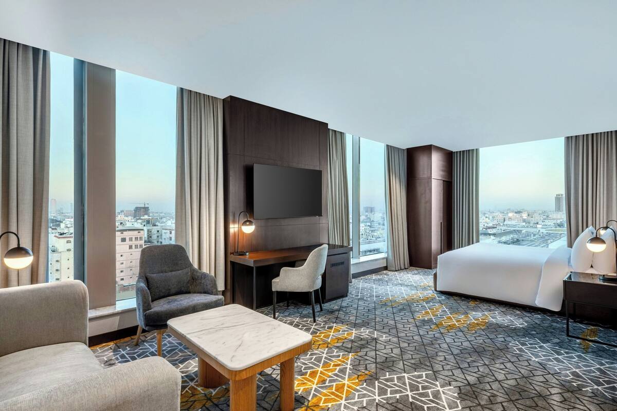 Een hotelkamer met een groot bed, een bureau, een televisie en uitzicht op de stad.