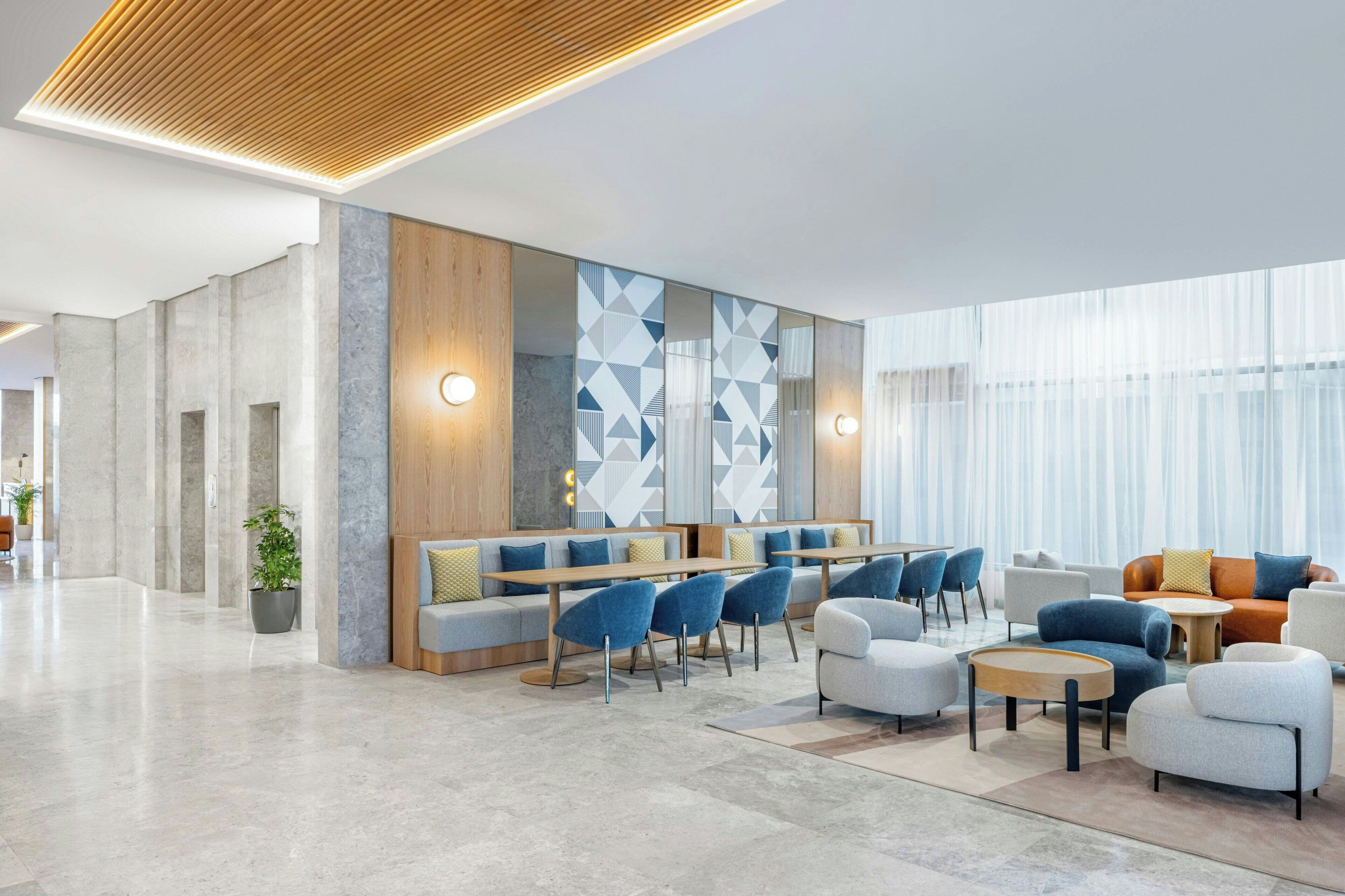 A spacious lobby with a modern seating area, a large wall with geometric patterns, and a large window providing natural light.