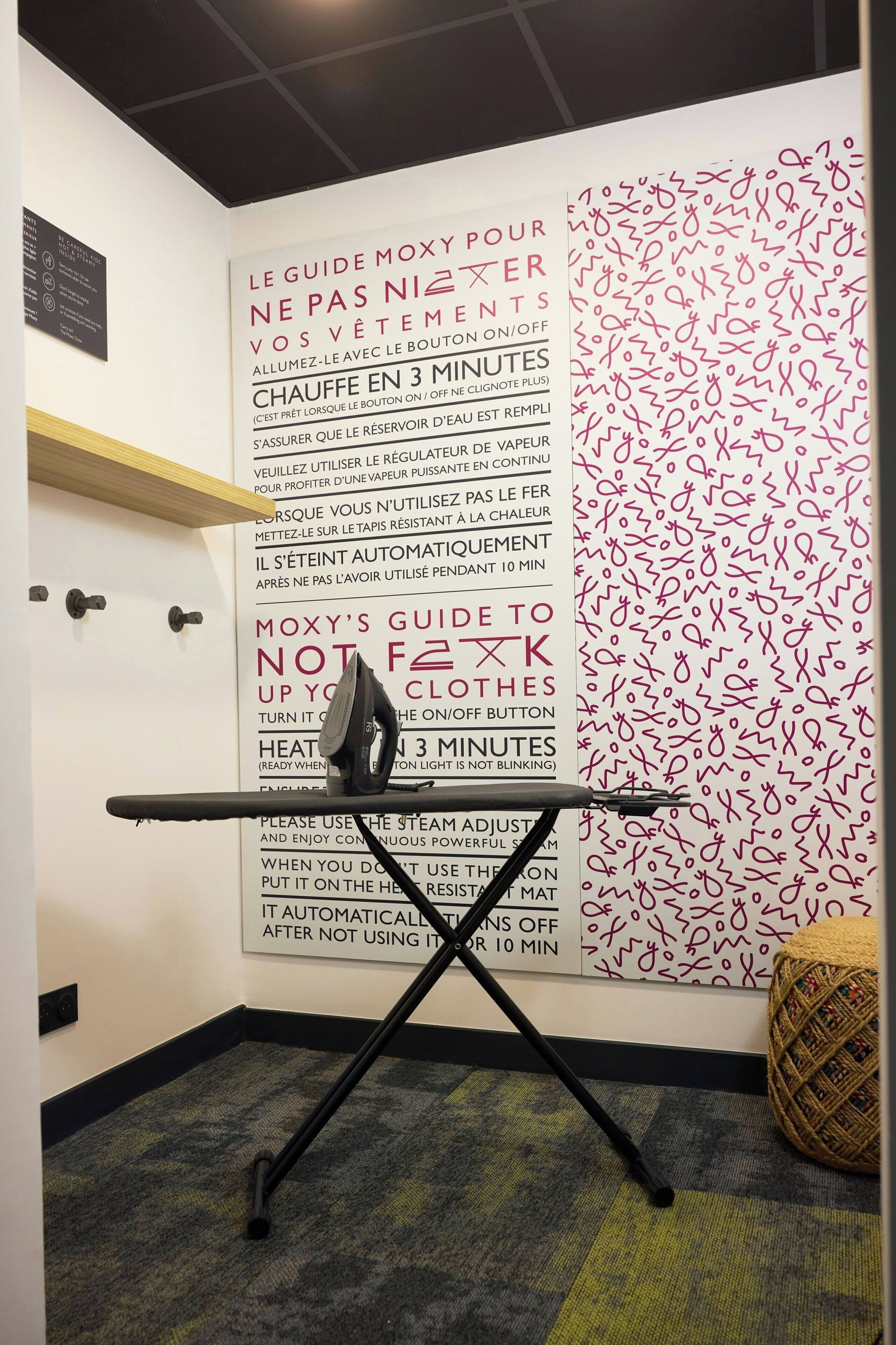 A room with a wall-mounted ironing board and a wall with safety instructions in French.