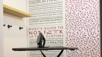 A room with a wall-mounted ironing board and a wall with safety instructions in French.