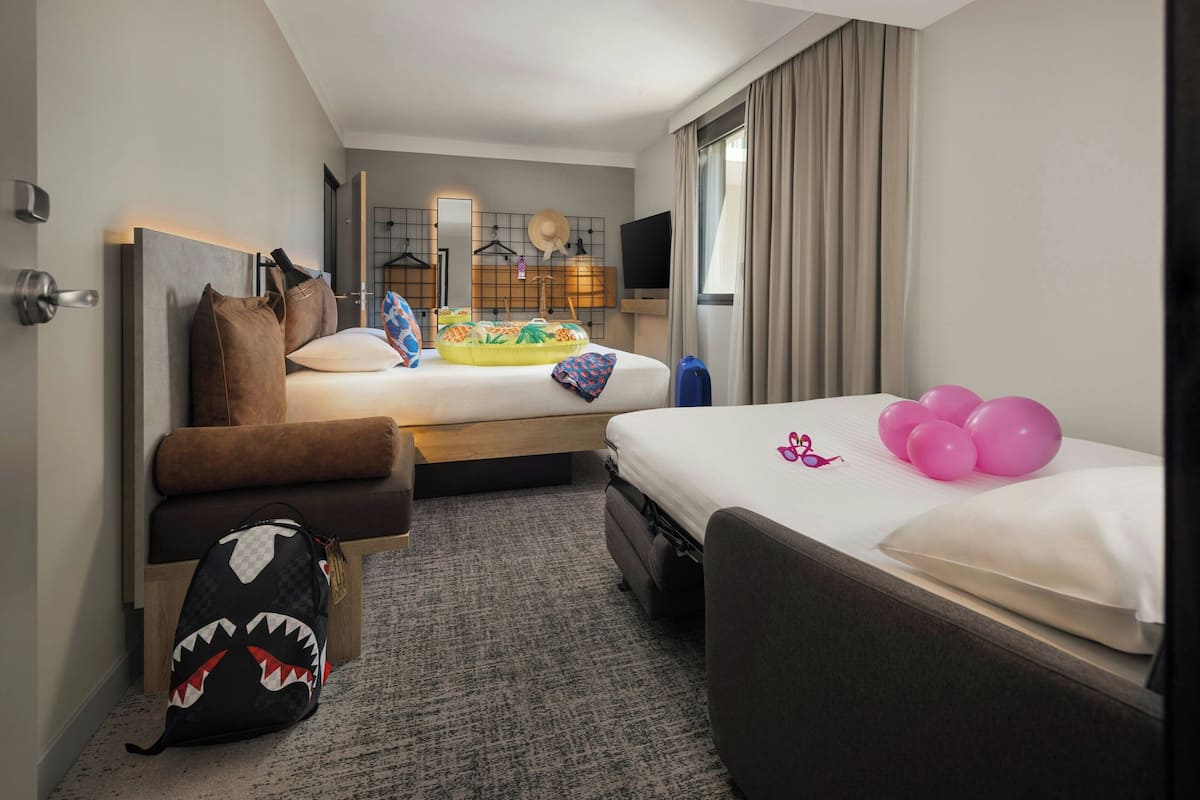A hotel room with two beds, a sofa, a small table, and a suitcase.