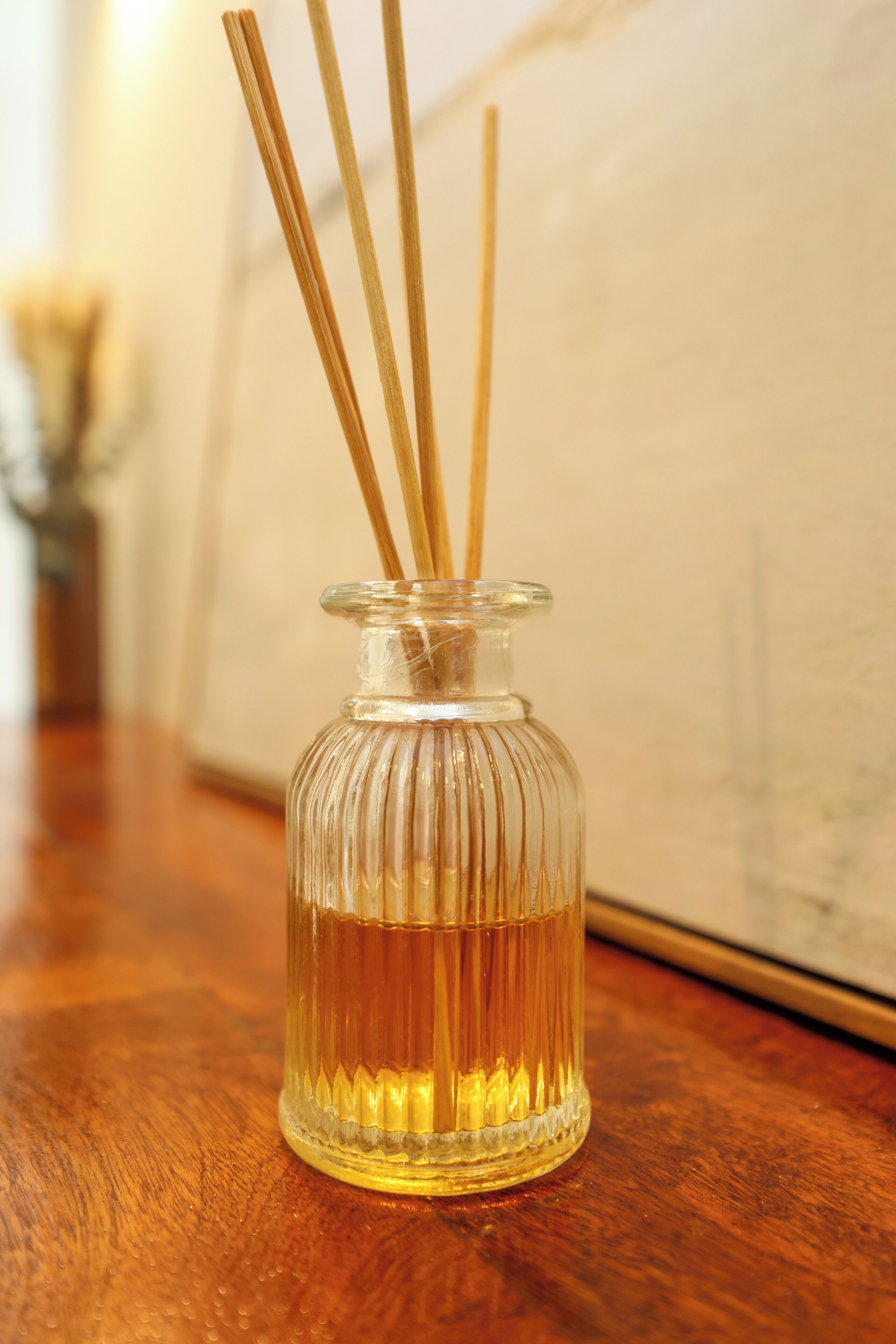 A clear glass bottle with a narrow neck and a wider base, containing a yellowish liquid and several wooden sticks.