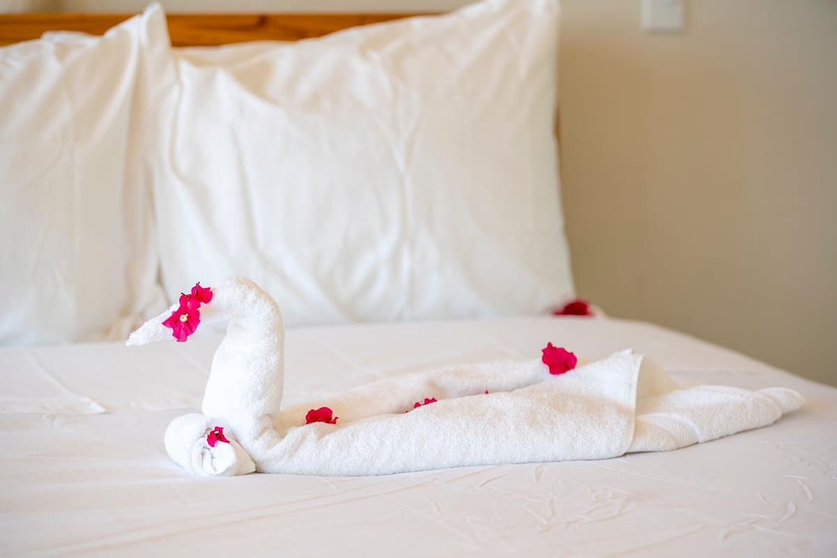 Una cama con sábanas blancas y un arreglo decorativo de toallas con forma de cisne y pétalos de rosa.