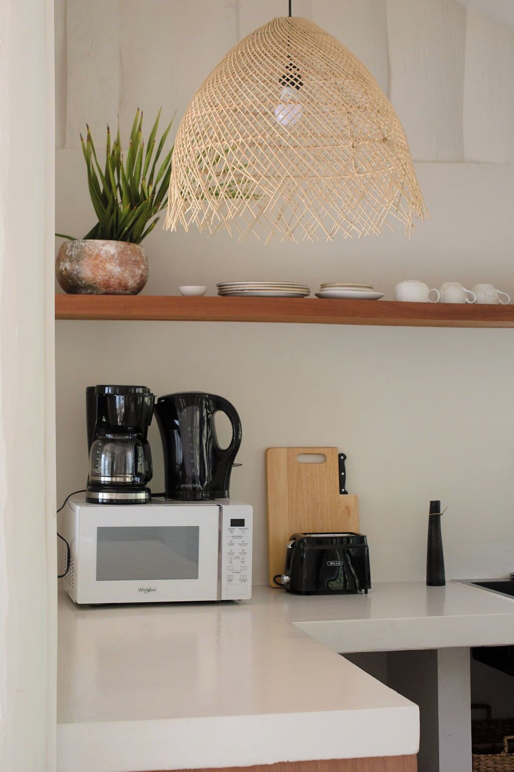 Uma cozinha com micro-ondas, cafeteira, torradeira e uma tábua de corte de madeira.