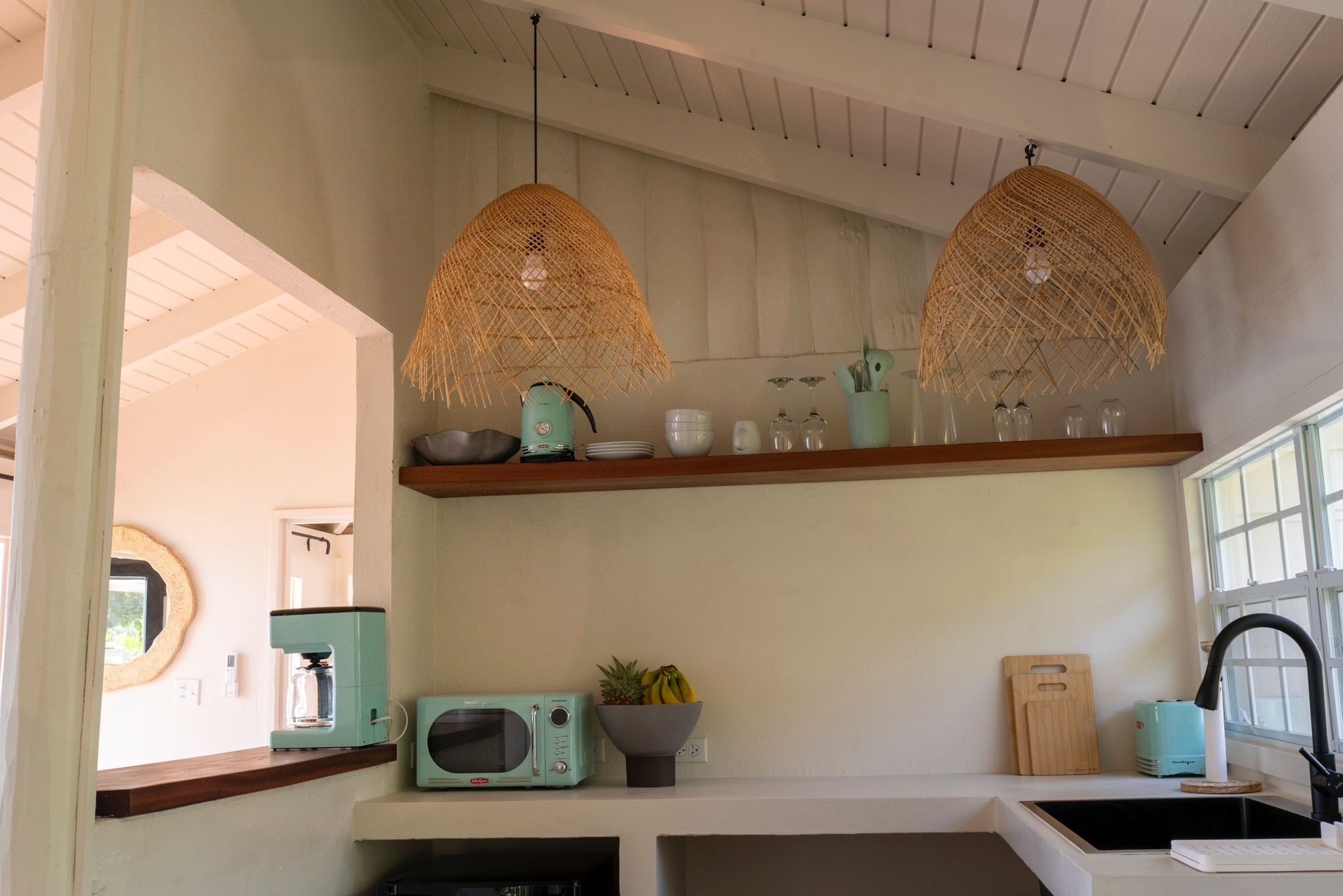 Una cucina con forno a microonde, macchina da caffè, una ciotola di frutta e lampade in vimini appese.