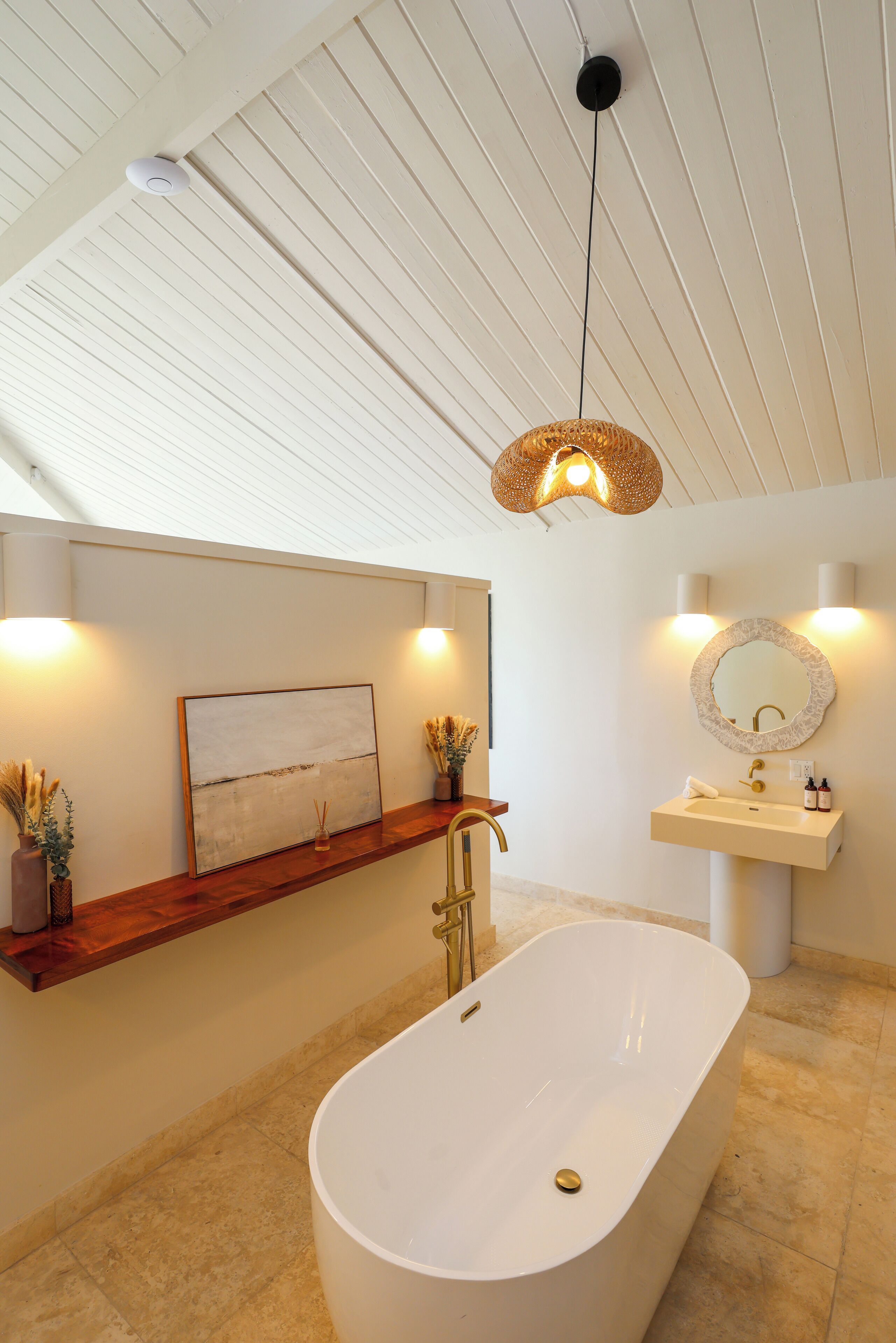 A modern bathroom with a freestanding bathtub, a wooden shelf with decorative items, a wall-mounted mirror, and a ceiling light fixture.