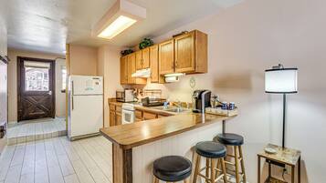 A kitchen with wooden cabinets, a stainless steel sink, a refrigerator, a stove, and two bar stools.