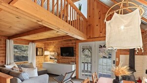 A cozy cabin interior with a wooden interior, a sofa, a dining table, and a hanging chair.