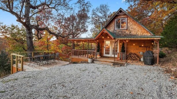 A cabin with a covered deck, a front porch, and a gravel driveway.