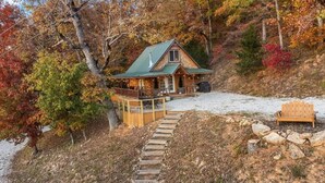 A cabin with a deck, a covered porch, and a stone staircase leading to the entrance.