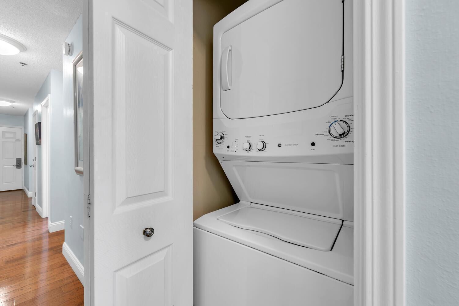 A laundry room with a front-loading washer and dryer, a door, and wooden flooring.
