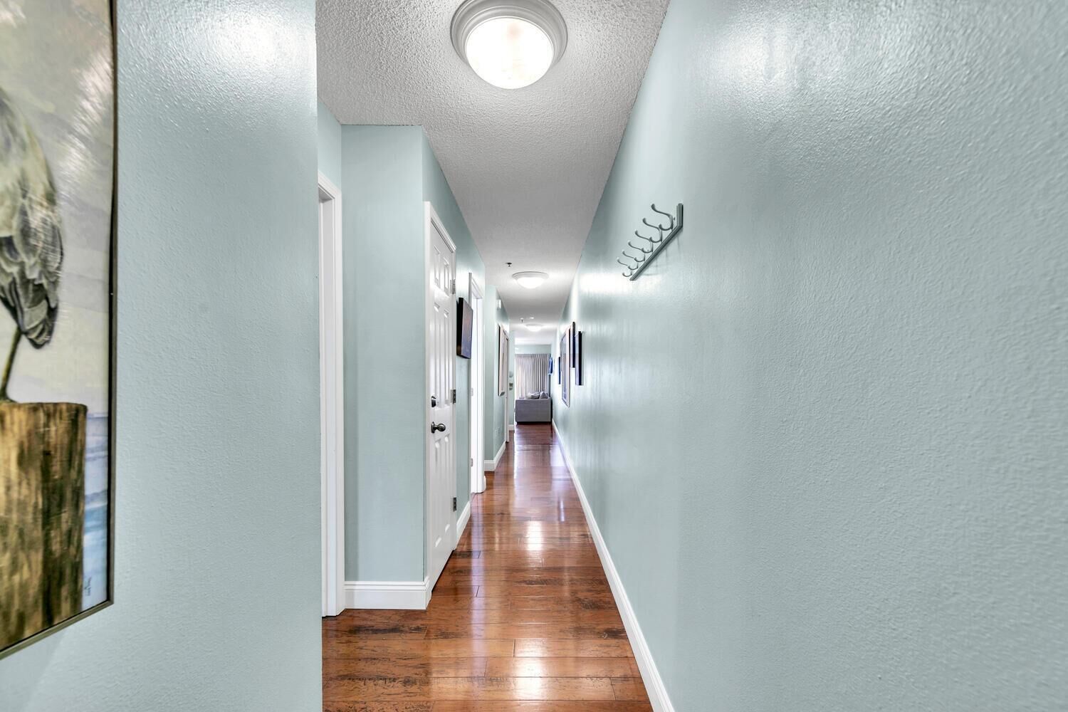 A hallway with light blue walls, wooden flooring, and a ceiling light.