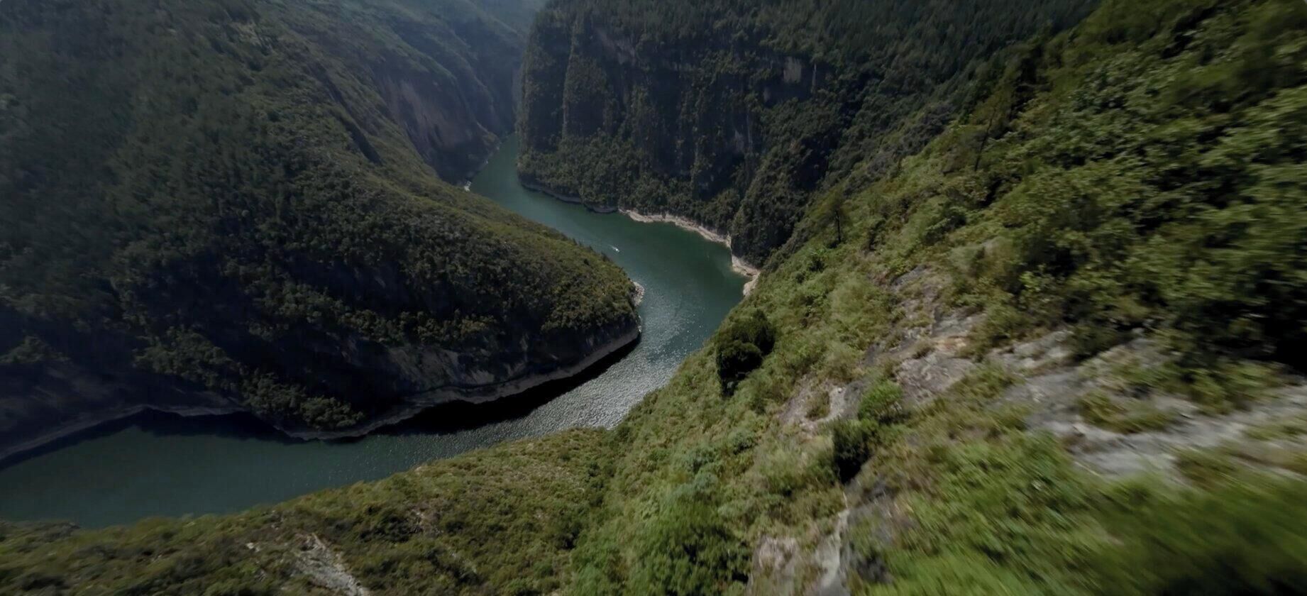 Un cañón con un río, abundante vegetación y un sendero estrecho.