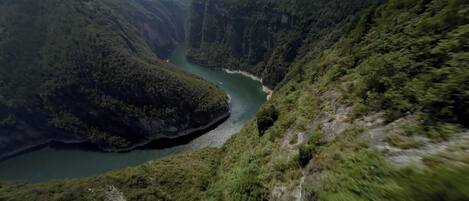 Un cañón con un río, abundante vegetación y un sendero estrecho.