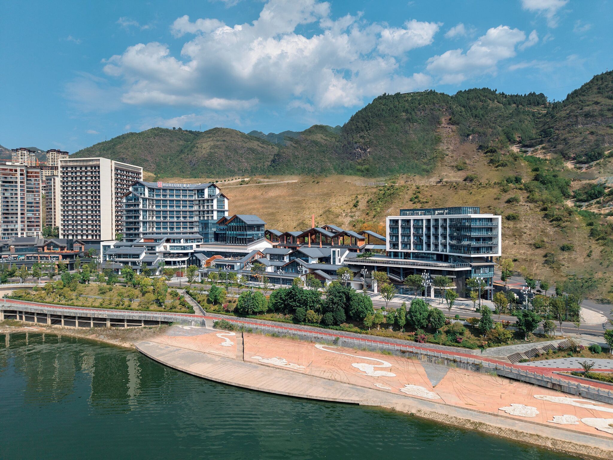 Un moderno complejo hotelero con varias torres altas, un paseo marítimo y colinas circundantes.