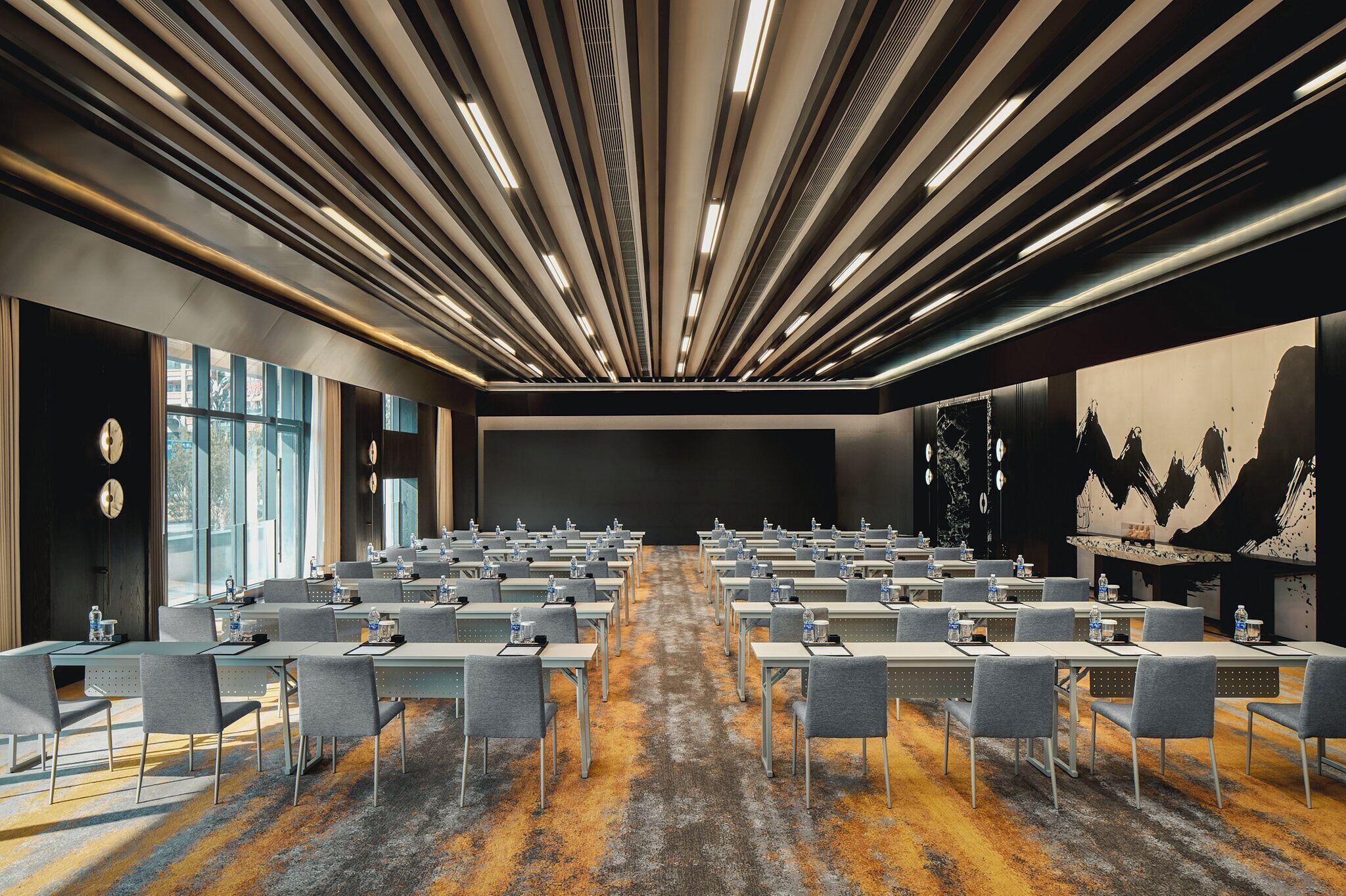 Un salón de conferencias con mesas y sillas dispuestas en filas, amplias ventanas y un diseño moderno del techo.