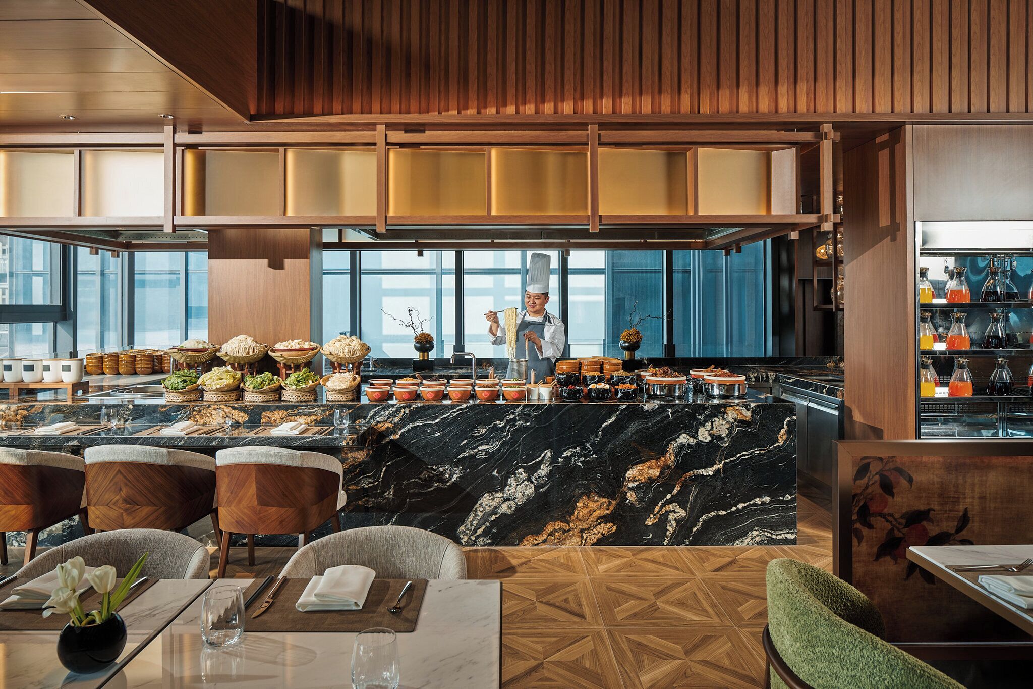 Un restaurante moderno con barra de mármol, mobiliario de madera y un chef preparando comida.